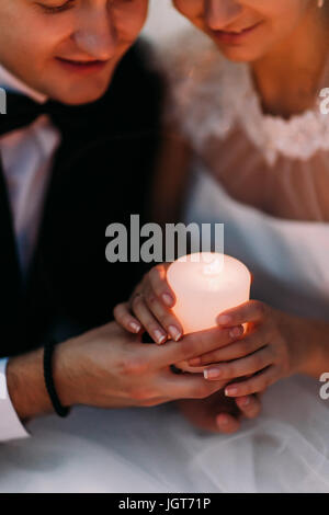 The close-up above view of the newlyweds` hands holding the shining candle. Stock Photo